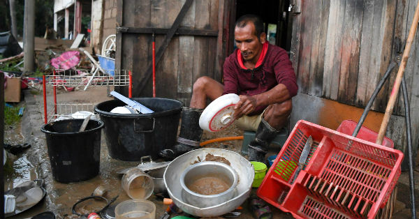 一名灾黎在清洗因洪水侵袭而被泥浆覆盖的餐具。