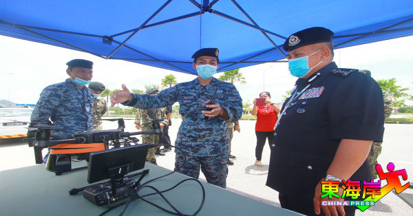 阿都加里尔（右）在丹绒隆坡行动管制军警路障中心，向空军祖海利（中）了解扩音广播无人机的操作流程。
