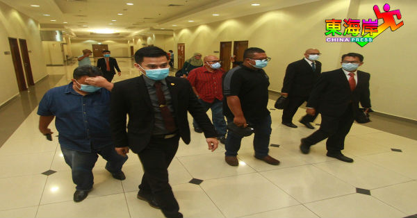 沙鲁阿兹祖慕沙（左）及慕哈末阿兹曼（左3）否认涉及投资油棕园地段骗局罪名后，由反贪会官员陪同离开法庭。