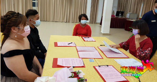 陈愫珊（右）为新人们主持婚姻注册仪式，众人全程遵守标准作业程序佩带口罩。