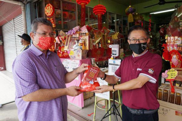 赛夫丁(左)派送新春福袋给关丹保健药行,由东主何国兴(右)接领。