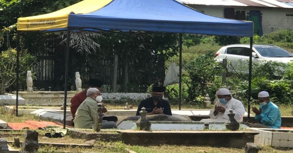 依斯迈（中）与兄长阿都马南耶谷（左）等人，围坐在双亲墓地，祈祷讼经。