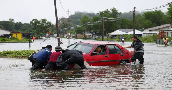 数名男子合力将涉水通过淹水区，却不慎撞下路旁沟渠的轿车“救离”灾区。