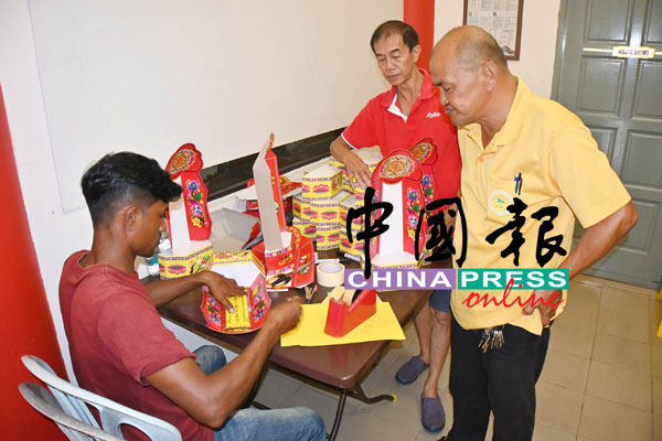 广义山理事何荣璋（右起）和财政李祤铭，亲自督导外劳进行摺叠灵位牌的工作。